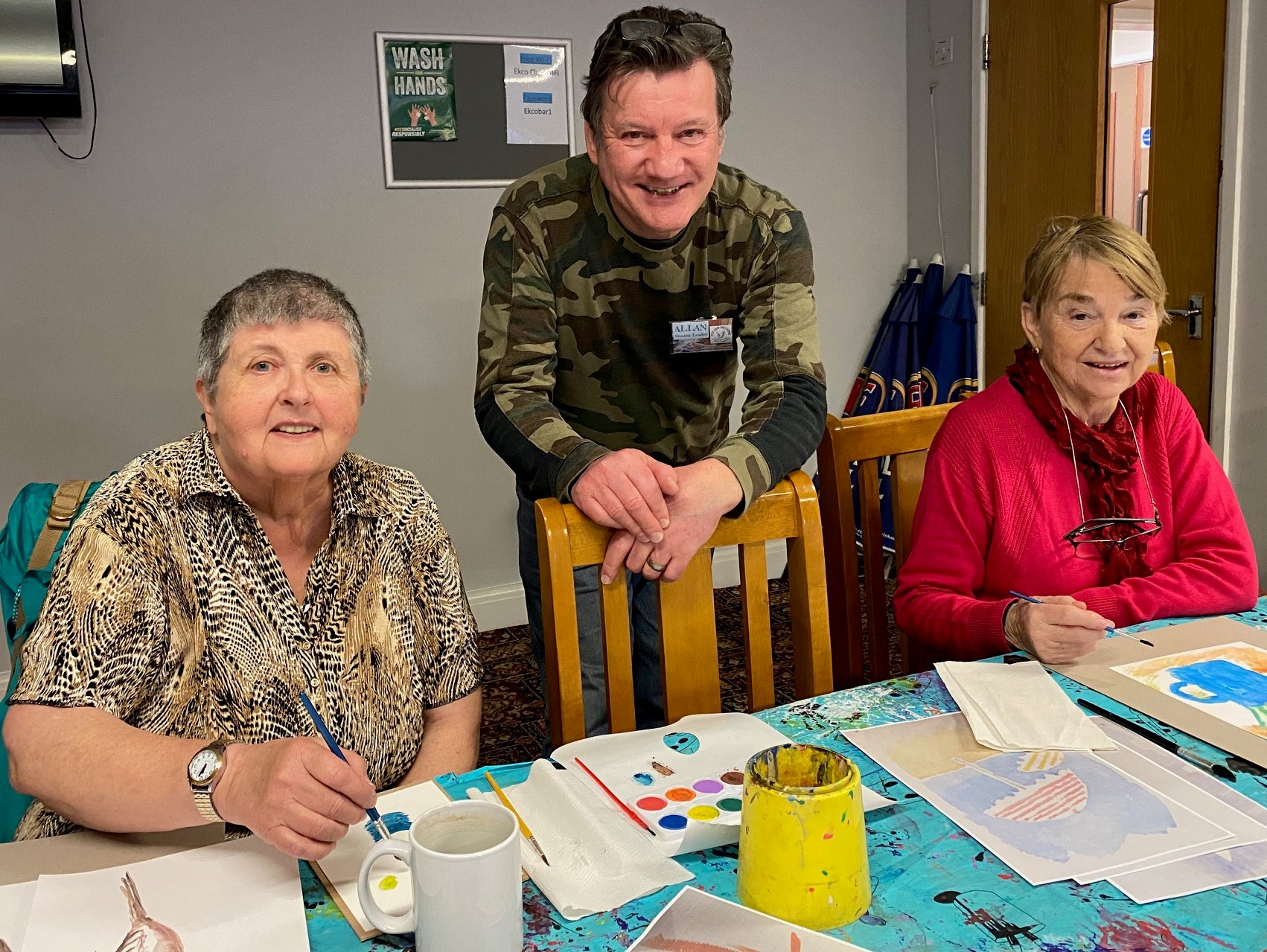 Photo shows Allan from the Art Ministry helping 2 clients with their painting.