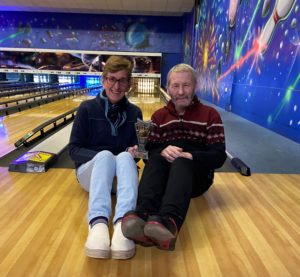 Photo shows Clare and Andrew sitting on the floor of the bowling lane with their trophy.