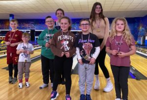 Photo shows visually impaired children with their friends and siblings wearing medals, posing for the camera on the bowling alley.