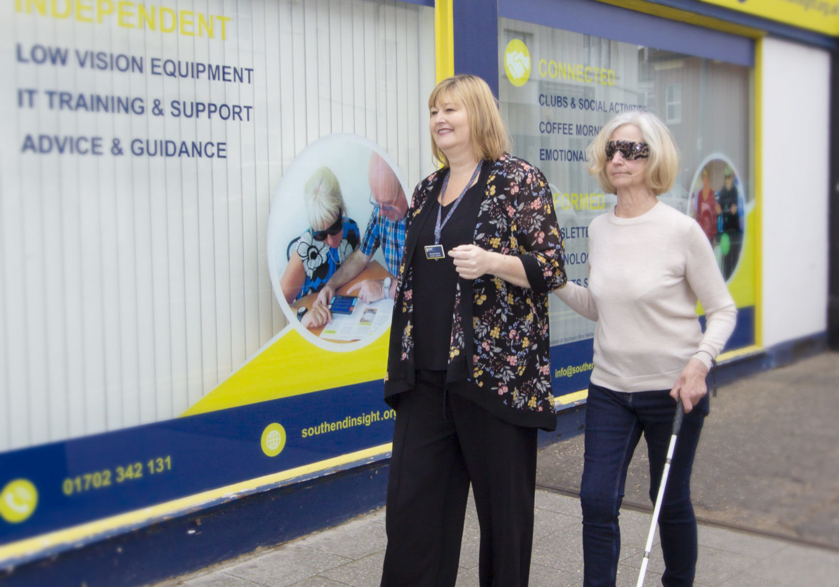 Picture shows sight loss awareness training in action, with a staff member guiding a visually impaired person with a cane.
